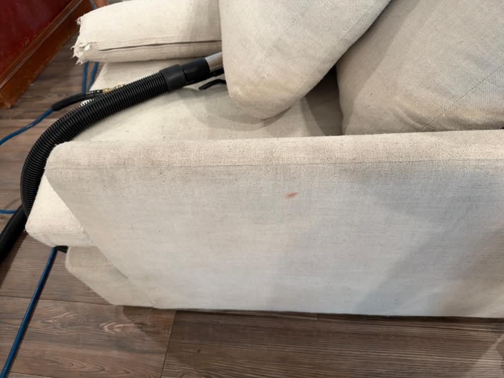 Upholstery cleaning wand extracting dirt from a cream fabric sofa